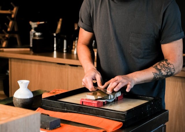 Various types of knife sharpeners, including a handheld sharpener, an electric sharpener, and a whetstone, displayed on a countertop.