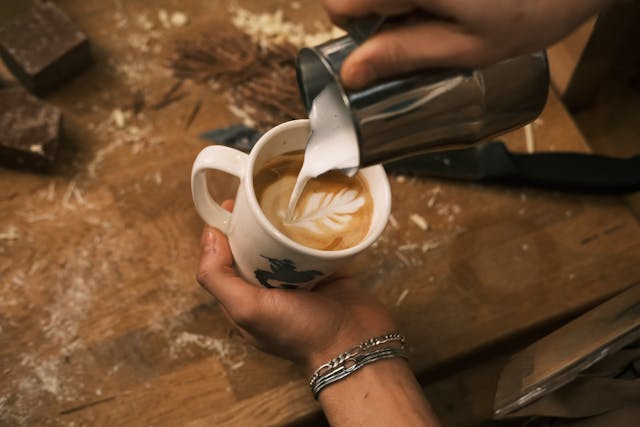 A barista pouring steamed milk into a cup of espresso, creating a beautiful latte art design.