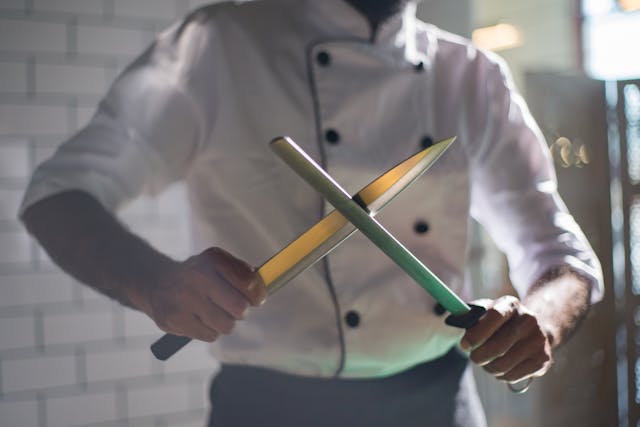  A professional chef using a honing rod to maintain a sharp knife in a well-lit kitchen.