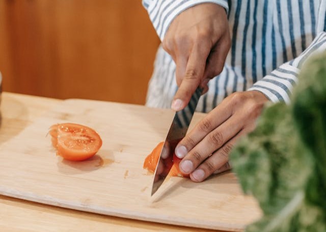 A person struggling to cut a tomato with a dull kitchen knife, creating a messy cut.